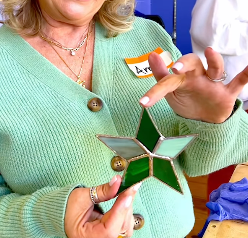 Photo of a student holding up a stained glass piece she created during a workshop. The piece is a green and white star.