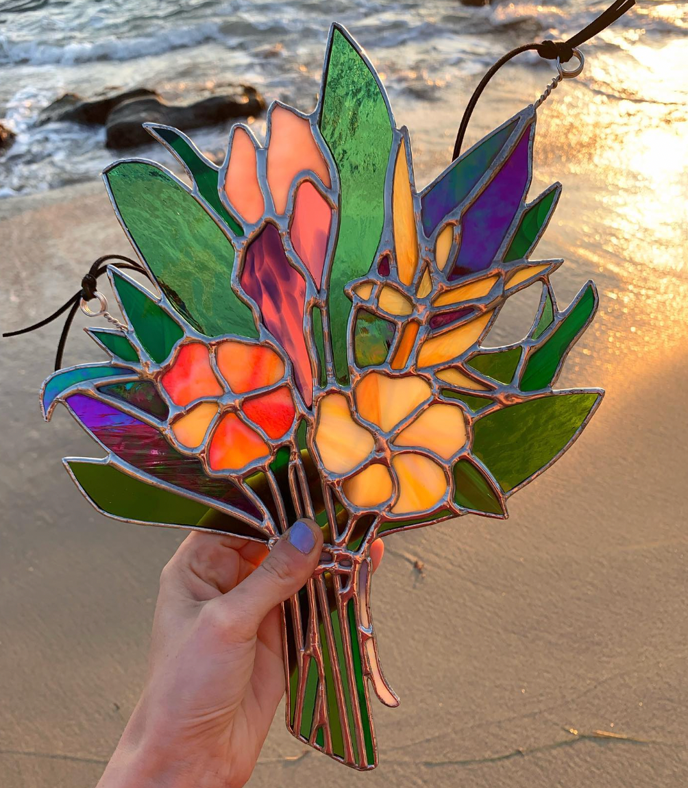 Photo of stained glass bouquet with several colors and flowers in it with the beach in the background