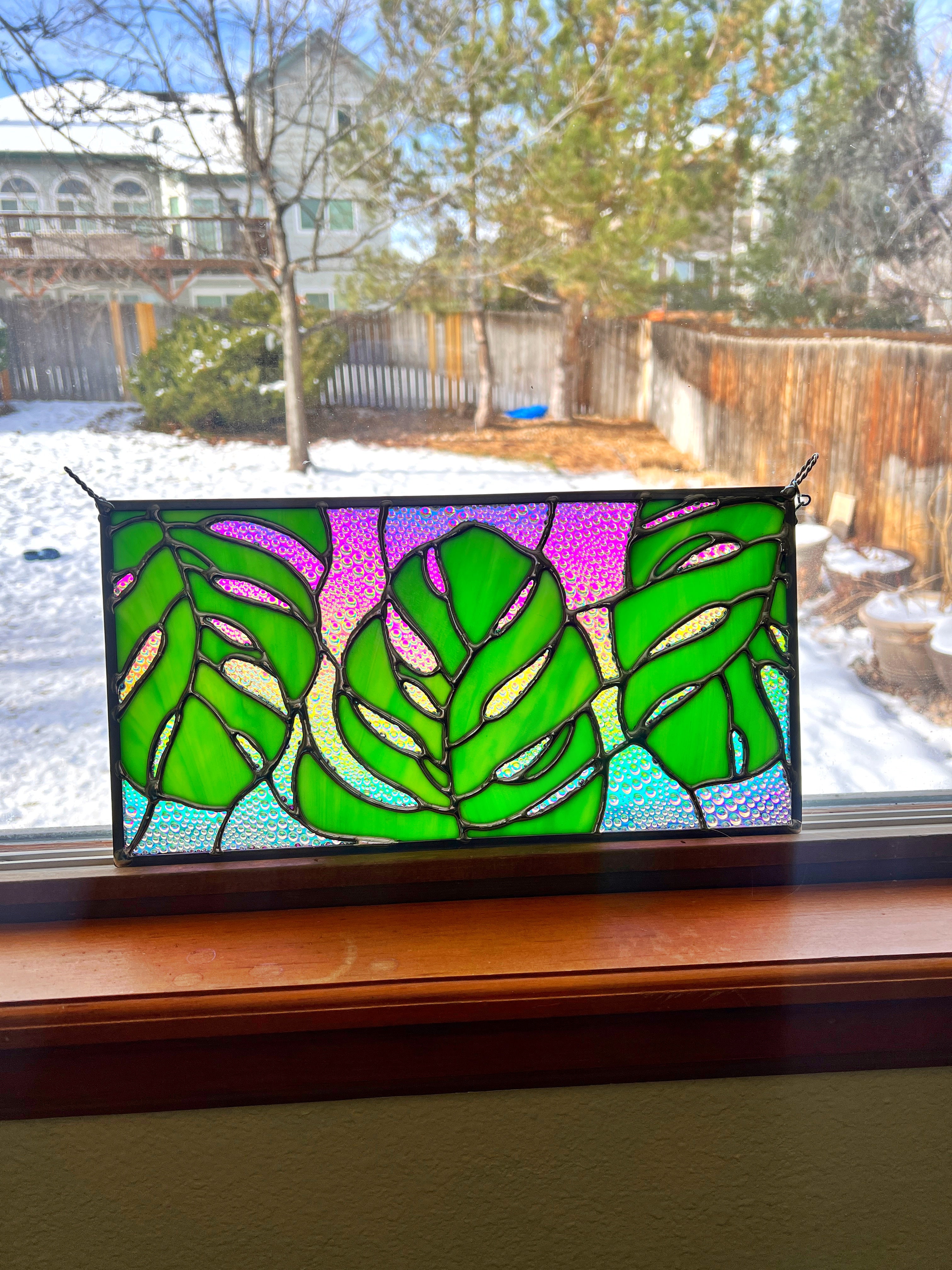 Rectangular stained glass piece with 3 monstera leaves and a rainbow background of color