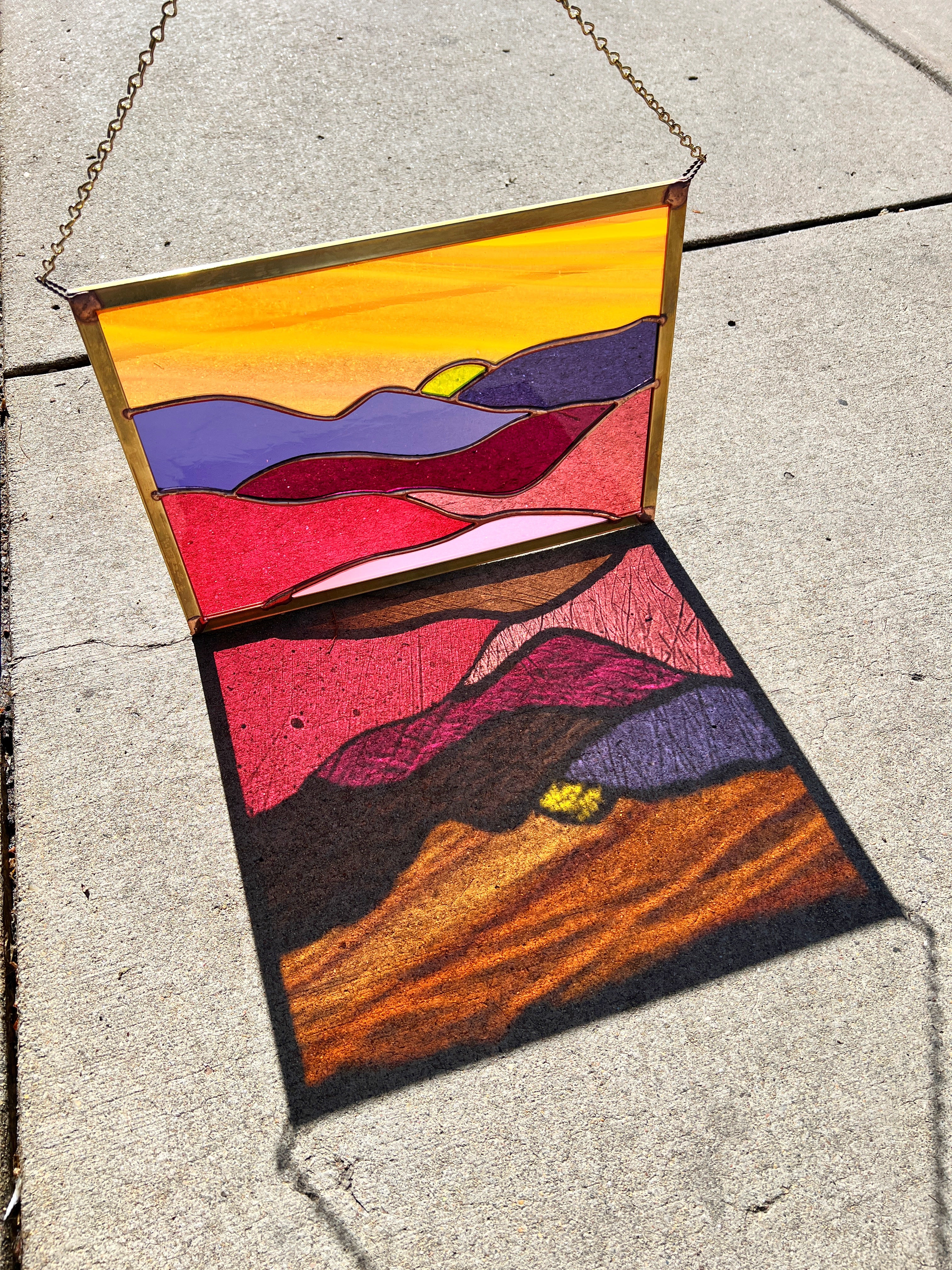 A colorful mountain scene in a square stained glass panel 