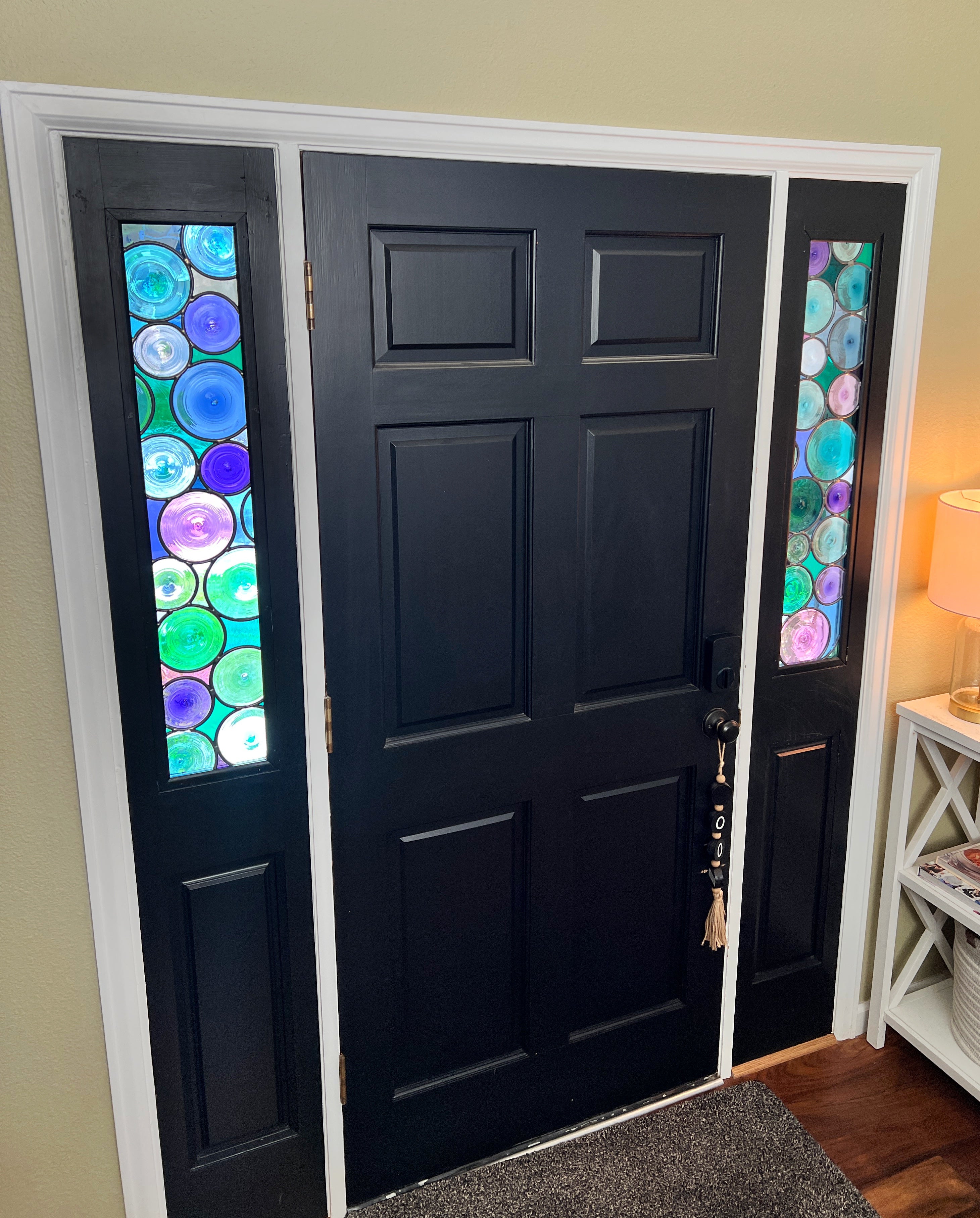 Picture of a black front door with two colorful side light stained glass windows on each side of the door