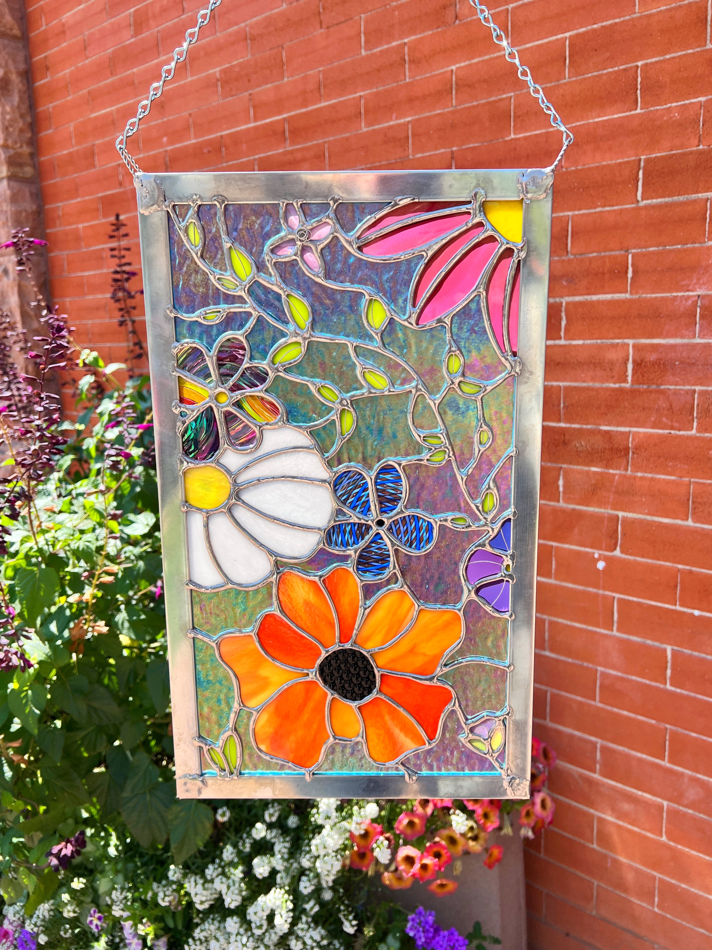 A large rectangle stained glass flower panel against a red brick background