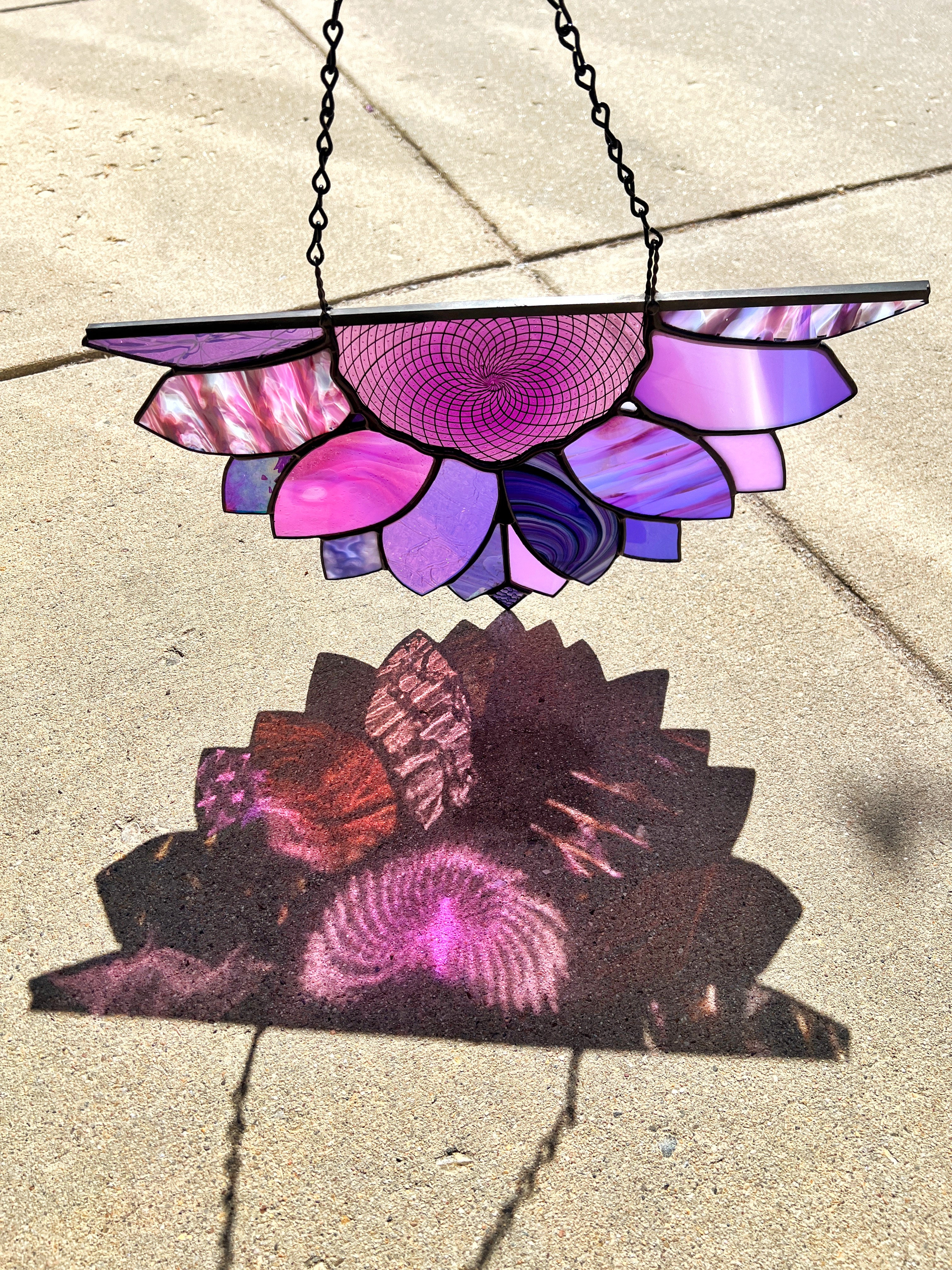 a stained glass purple half sunflower with a refraction of color on the concrete. 