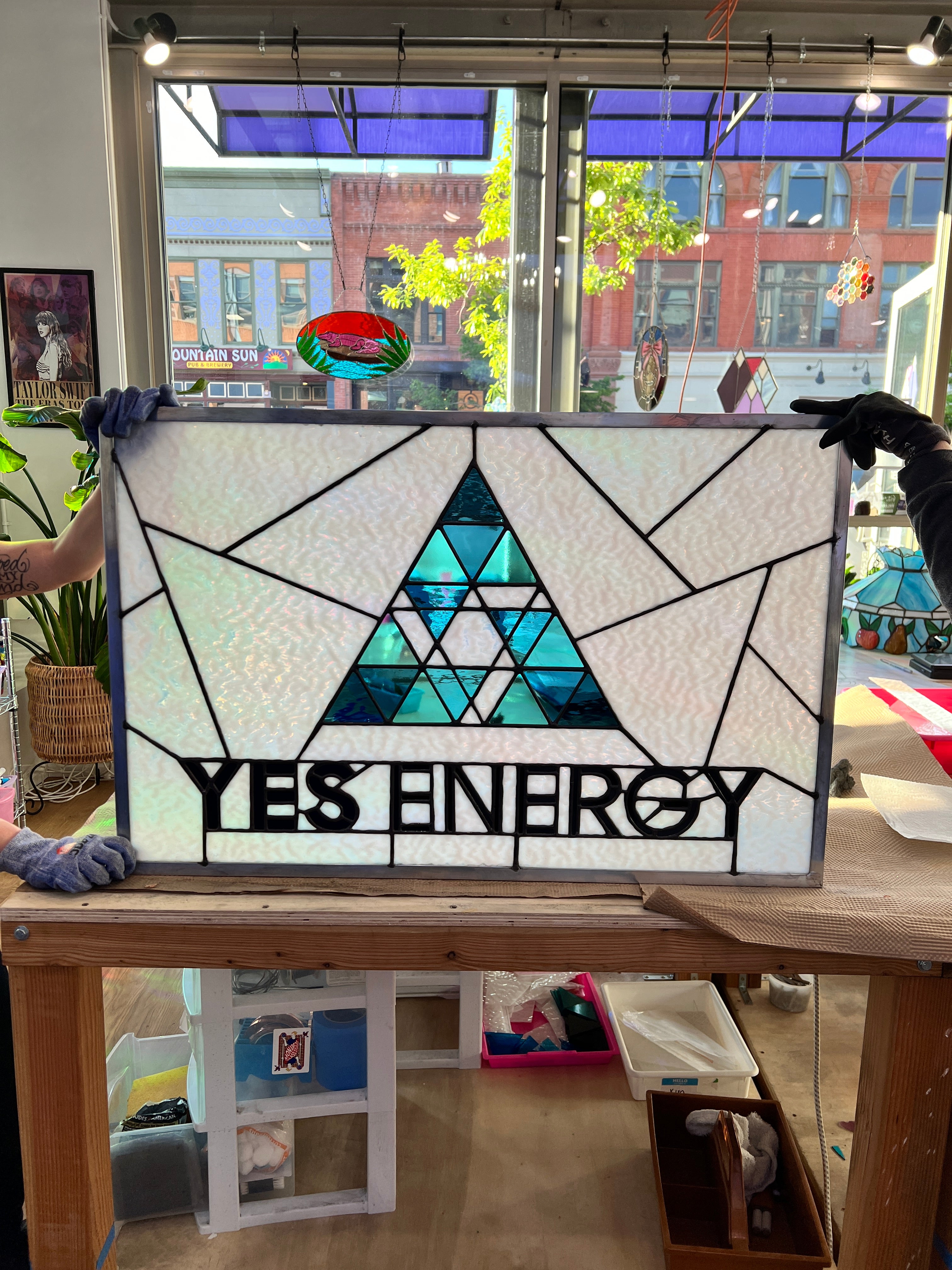 A large stained glass panel with a geometric triangle in the middle with the words yes energy in black below. 