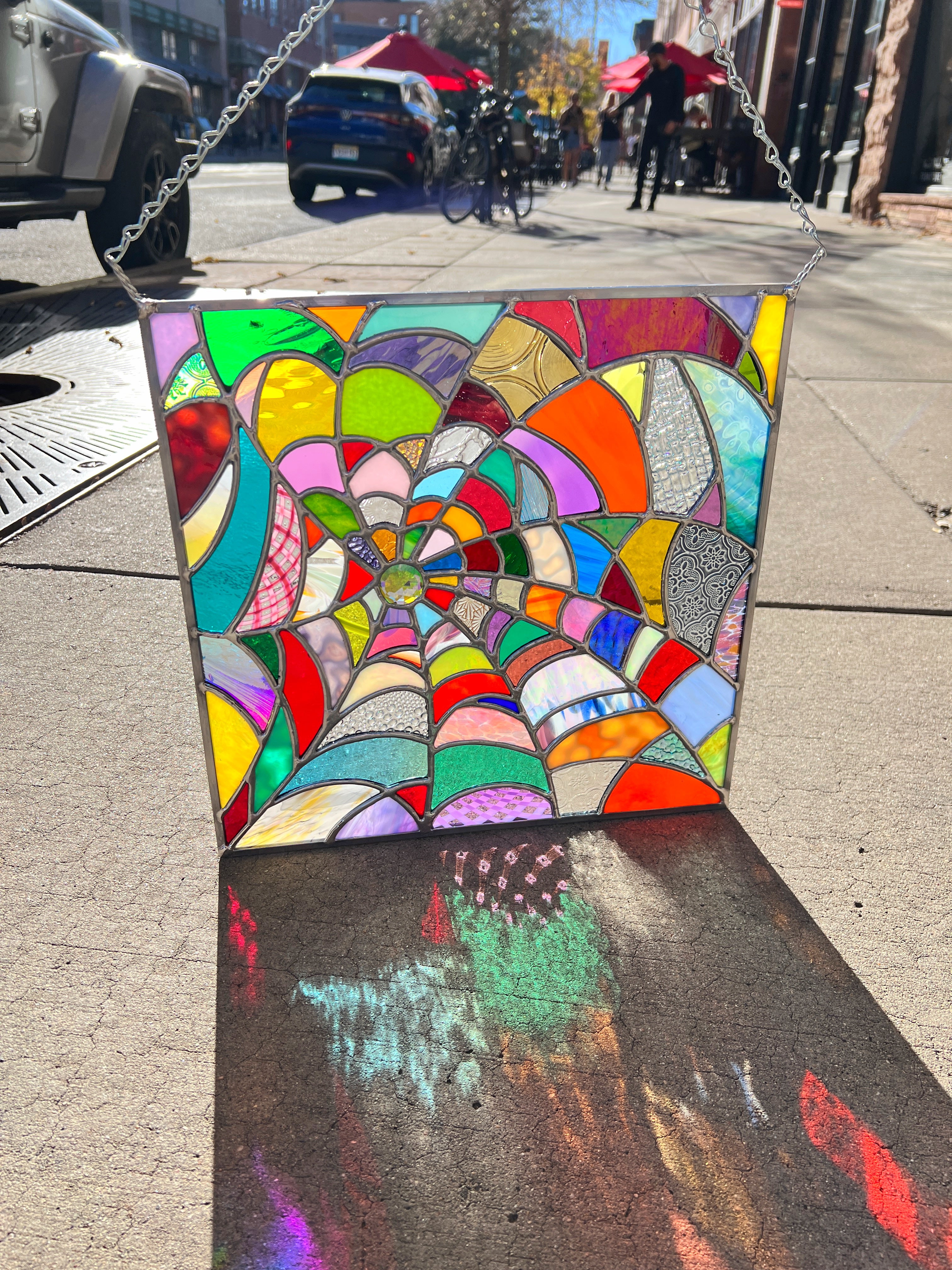 Image of a square stained glass panel - a spider web in rainbow colors